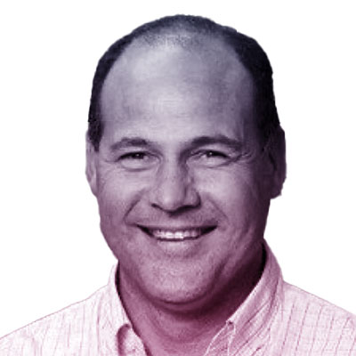 A man with short hair smiles at the camera, wearing a light-colored collared shirt against a white background.